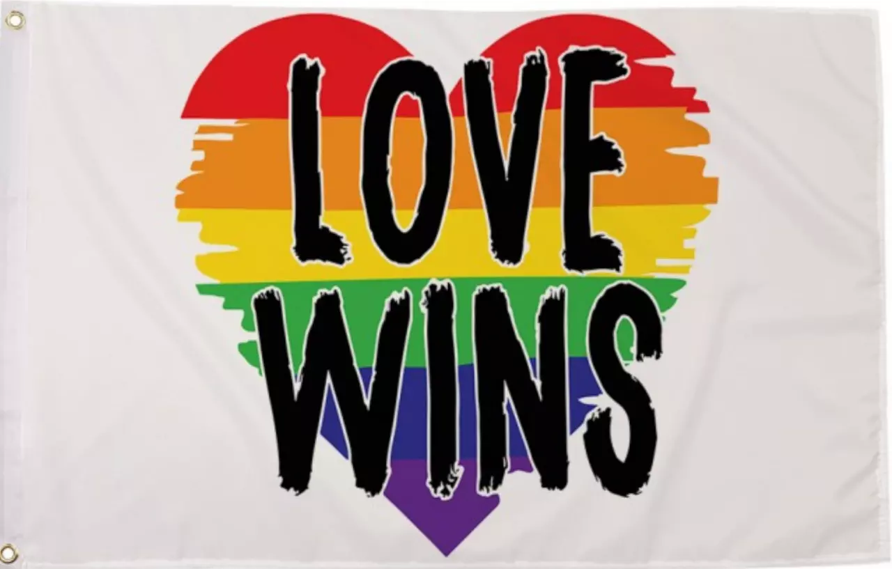 Die 'Love Wins' Regenbogenflagge mit einem herzförmigen Zentrum aus Regenbogenstreifen auf einem weißen Hintergrund. Die Streifen im Herzen sind fransig gestaltet, was einen Hauch von Sanftheit und Tiefe verleiht. Die Botschaft 'LOVE WINS', in schwarzen G