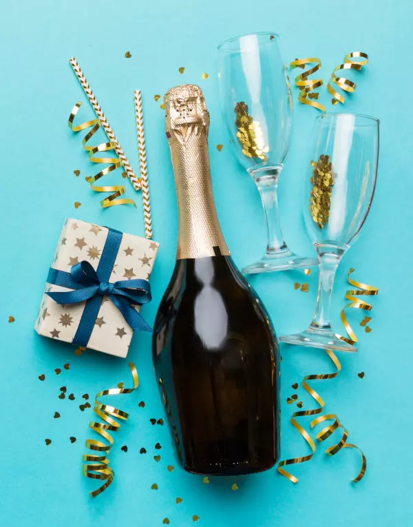 Eine stilvolle Sektflasche und Sektgläser auf einem hellblauen Hintergrund, liebevoll fotografiert, daneben ein Geschenk, perfekt für festliche Anlässe und Feierlichkeiten, präsentiert von flaggenmeer