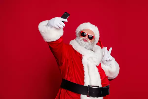 Ein cooler Weihnachtsmann mit Sonnenbrille macht ein Selfie vor einem roten Hintergrund, verkörpert einen trendigen und lässigen Weihnachtsgeist, humorvoll präsentiert von flaggenmeer